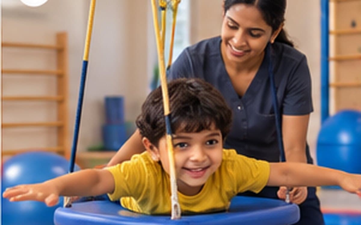 A boy lies across a platform swing with his arms outstretched, grinning, while an occupational therapist steadies the rope behind him.